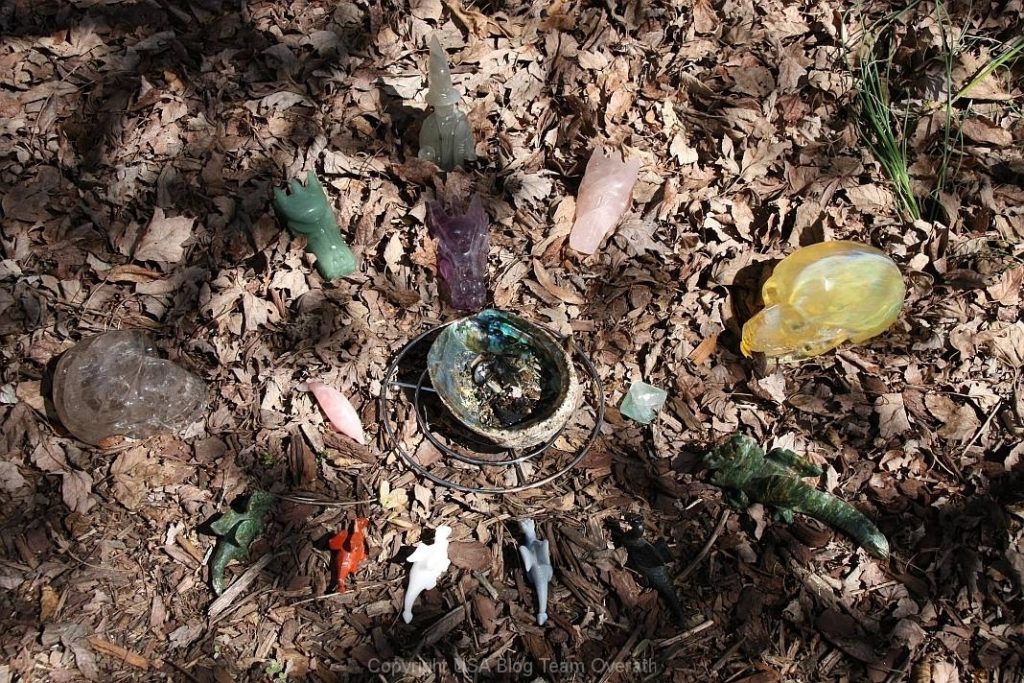 Ein Kreis aus Glasobjekten, die an Kristallschädel erinnern und auf dem Boden verstreut sind.